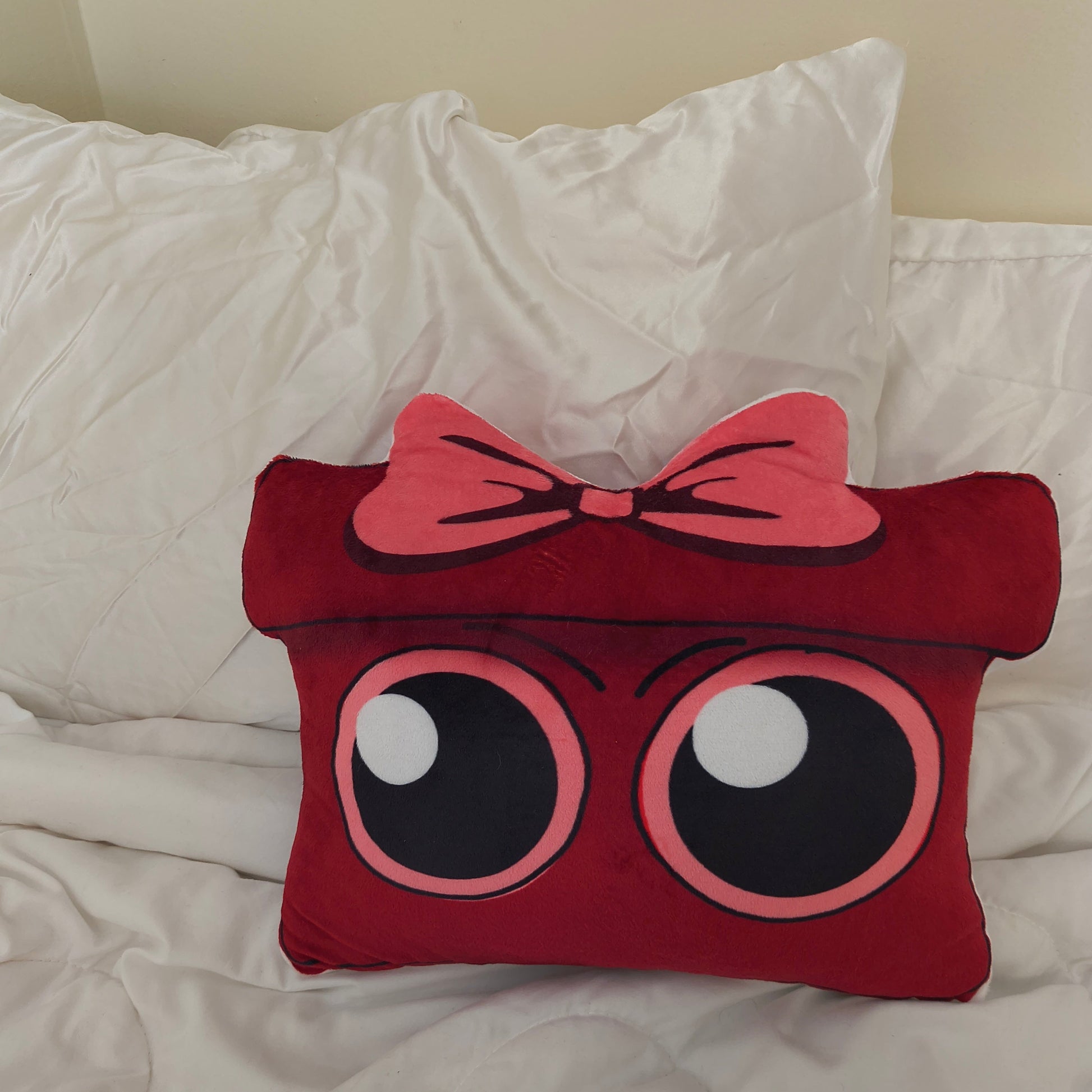 Red pillow with eye design and pink bow on a white bed